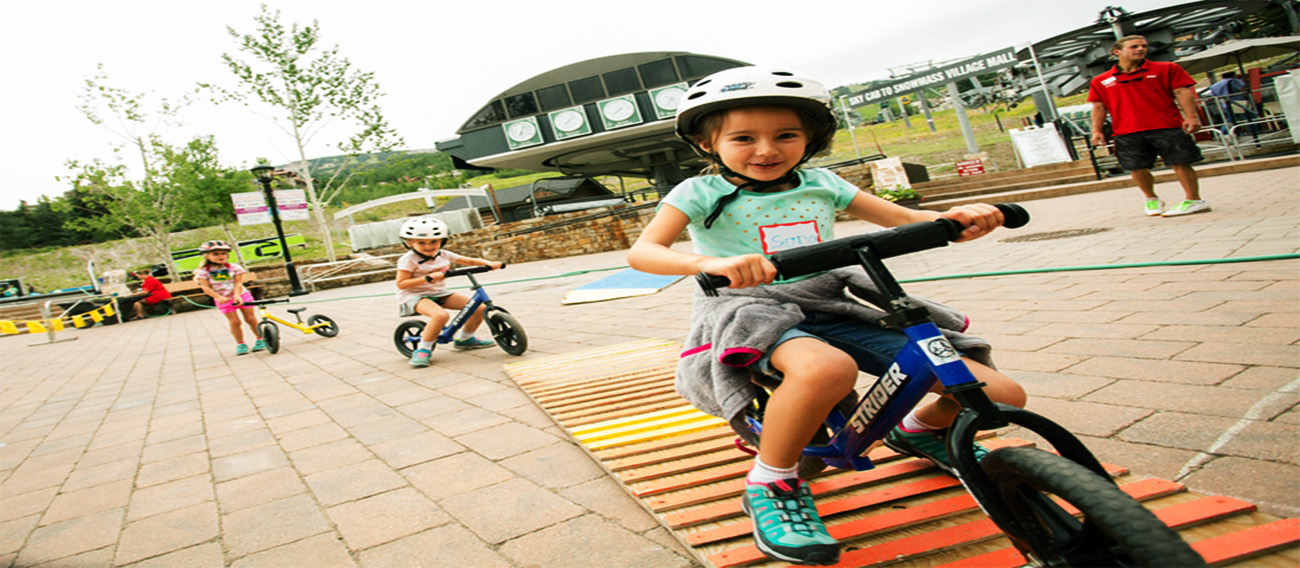 Snowmass Village: kids in plaza on push bikes with safety gear 