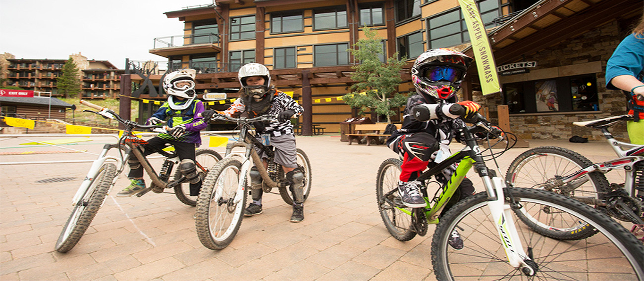 Kids on mountain bikes in Snowmass Base Village plaza next to ski lift on