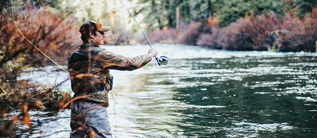 Man fly fishing on Aspen riverbank in Autumn.