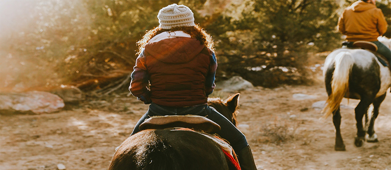 Women riding horseback going down trail